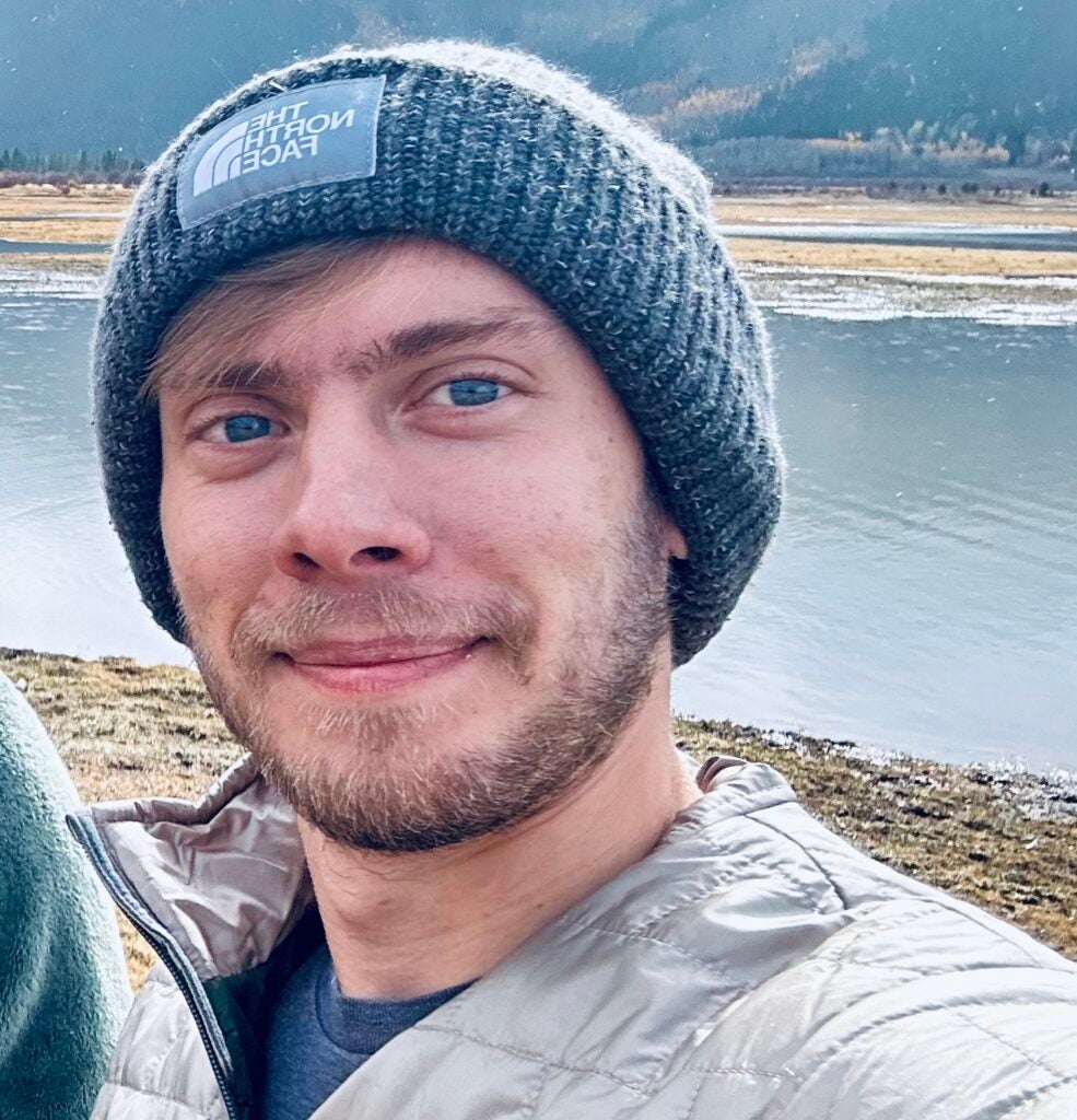 Colin Langton in hat standing in front of water.