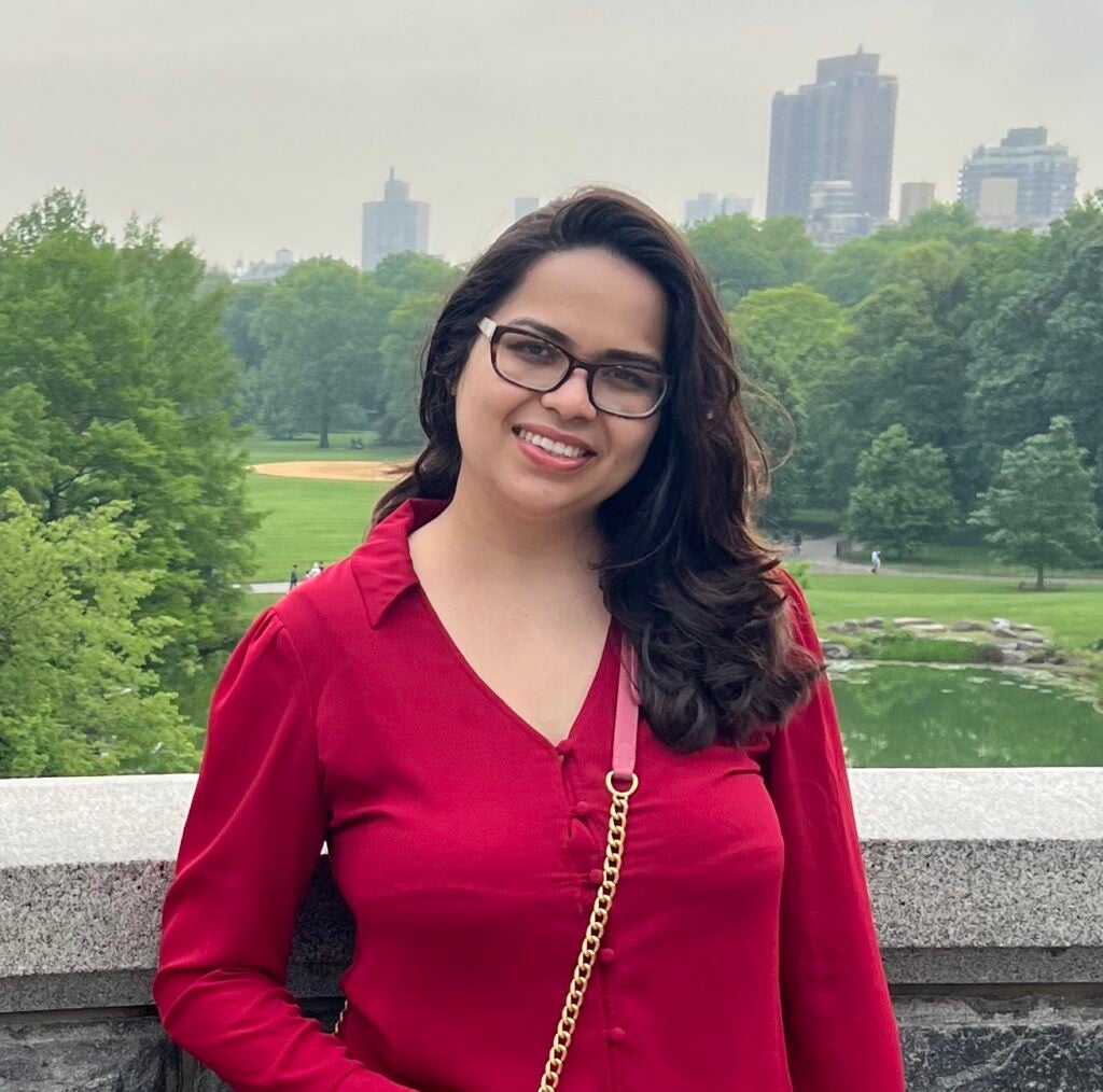 Raheen in red shirt standing in front of city skyline. 